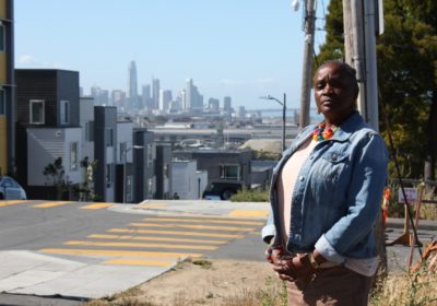 Resident Lottie Titus stands next to a street with San Francisco skyline in the background