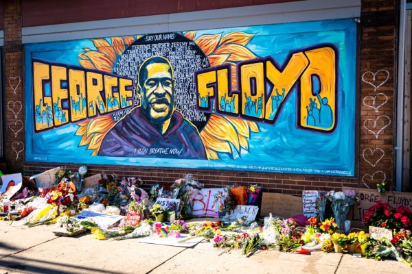 A mural of George Floyd surrounded by flowers and protest signs.