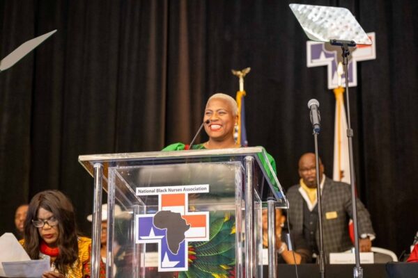 Smiling Black woman stands at podium in front of crowd